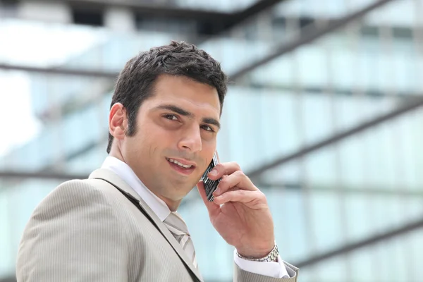 Entrepreneur using a cellphone outside a mirrored building — Stock Photo, Image