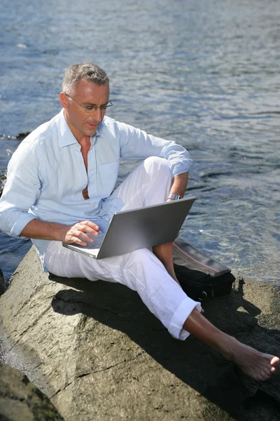 Людина використовує свій ноутбук біля водного краю — стокове фото