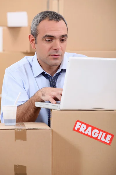 Entrepreneur with laptop amid removal boxes — Stock Photo, Image