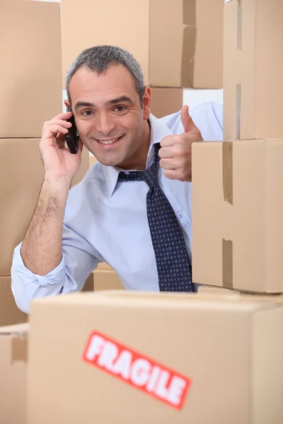 Happy man on phone behind stacks of boxes — Stock Photo, Image