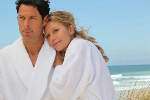 Par stod på stranden bär bad kappor — Stockfoto