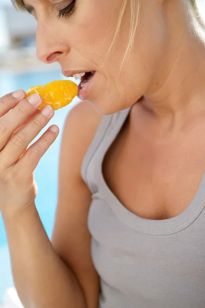 Γυναίκα τρώει ένα πορτοκαλί δίπλα στην πισίνα — Φωτογραφία Αρχείου