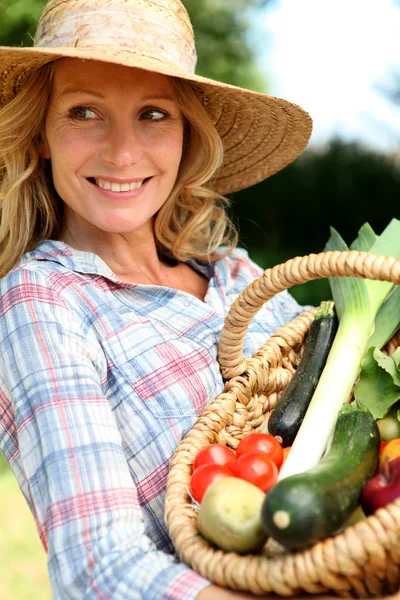 Vrouw met een stro hoed, bedrijf mand van groenten. — Stockfoto