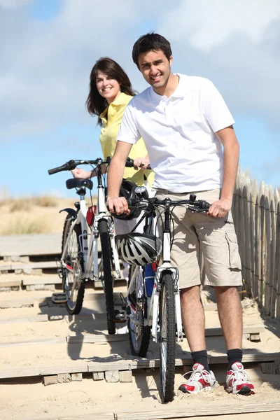 Coppia che porta le bici in spiaggia Immagine Stock