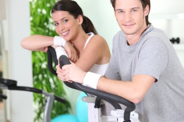 Two young resting on cardio machines clipart