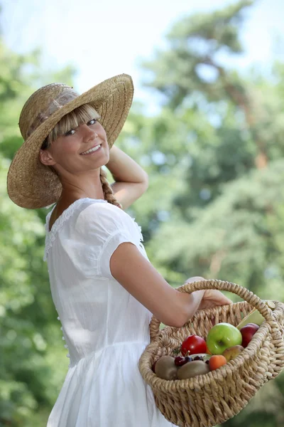 Літня жінка в солом'яному капелюсі тримає кошик з фруктами — стокове фото