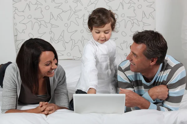 Föräldrar och dotter i sängen med laptop — Stockfoto