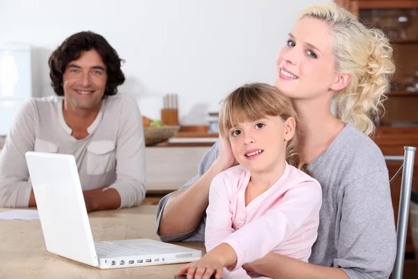 Родители и ее дочь улыбаются на кухне, компьютер на столе — стоковое фото