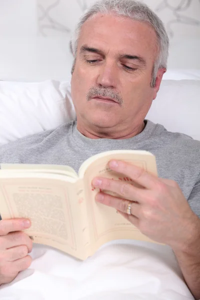 Dojrzały człowiek czytania książki w łóżku — Zdjęcie stockowe