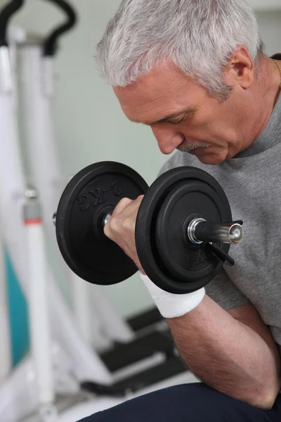 Mature white-haired man lifting weight in sports room — Stock Photo, Image