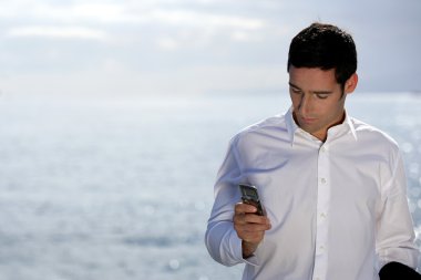 Man sending an SMS by the water's edge clipart