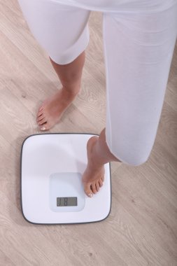 Cropped shot of a woman stepping a pair of scales clipart