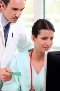 Doctor and nurse looking up a French Carte Vitale on a computer clipart