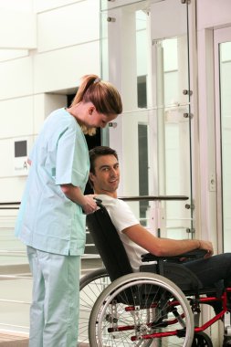 Nurse and patient in wheelchair in front of a lift clipart