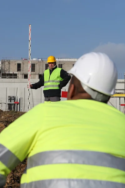Trabalhador da construção civil observando seu colega usando um medidor — Fotografia de Stock