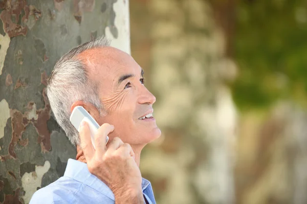 Grey-haired man with mobile telephone stood by tree — Stock Photo, Image