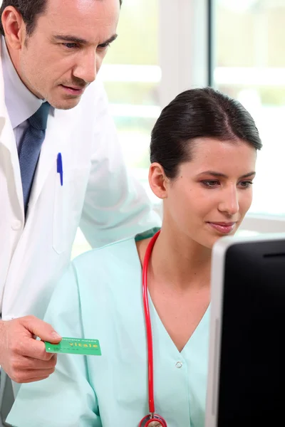 Doctor and nurse looking up a French Carte Vitale on a computer — Stock Photo, Image