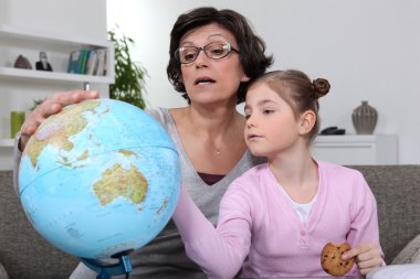 Woman looking at a globe with her granddaughter clipart