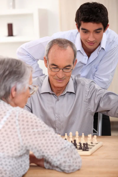Молодой человек смотрит, как пожилая пара играет в шахматы — стоковое фото