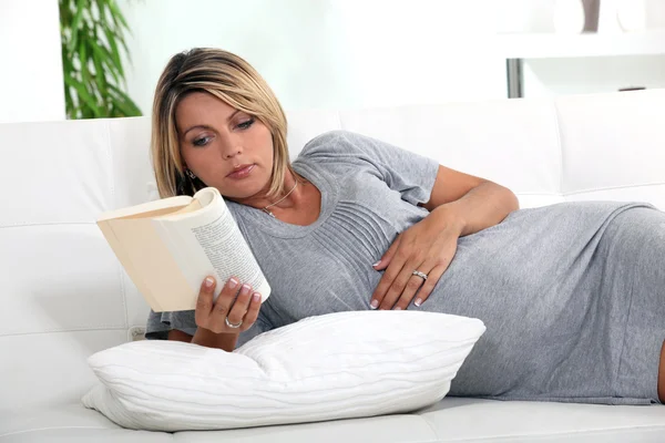 Mulher grávida deitada em um sofá lendo um livro — Fotografia de Stock