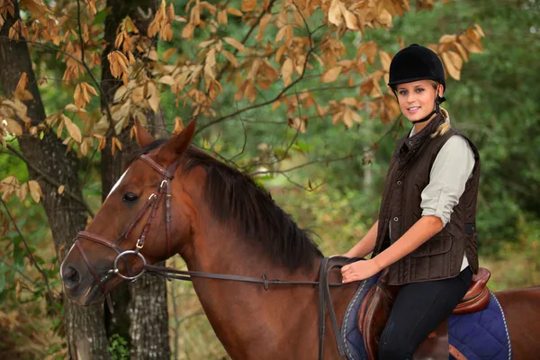 Mujer joven montando un caballo a través del bosque — Foto de Stock