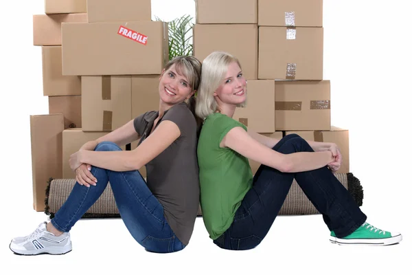 Mulheres sorridentes sentadas na frente de pilhas de caixas — Fotografia de Stock