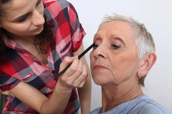 Woman applying makeup to an older lady — Stok fotoğraf
