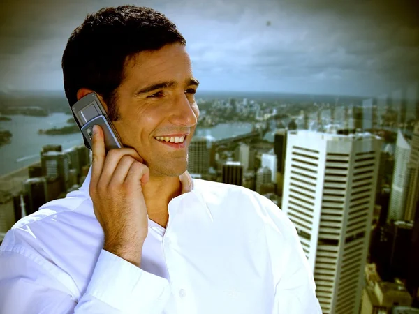 Empresário sorridente de cabelos escuros fazendo uma chamada contra o fundo urbano — Fotografia de Stock