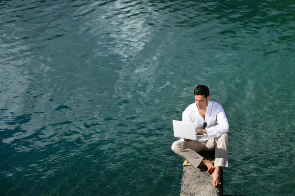 Человек сидит над водой с ноутбуком — стоковое фото
