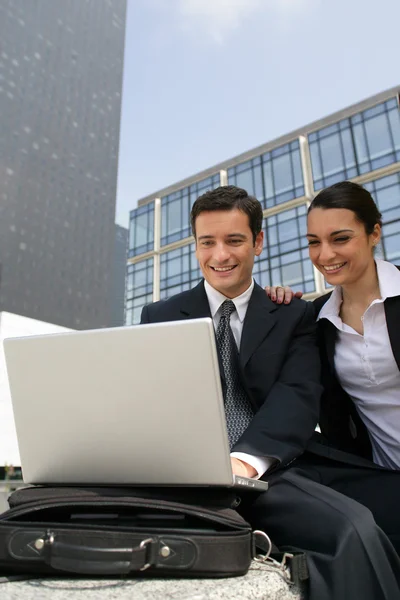 Businessman and businesswoman laughing in front of a laptop outdoors — Stock Photo, Image