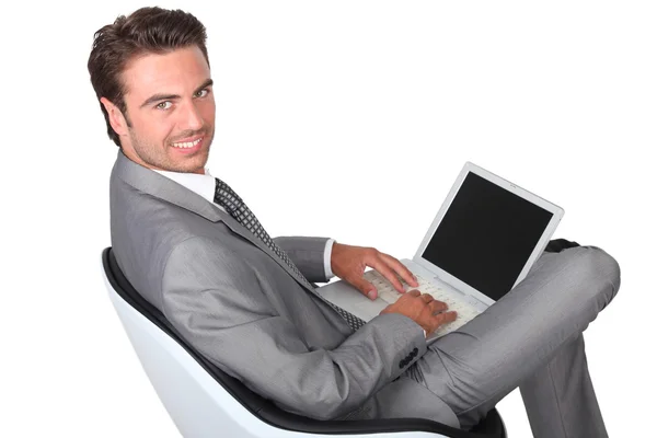 Элегантный бизнесмен, сидящий в кресле и работающий над ноутбуком — стоковое фото