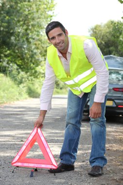 Man in fluorescent vest putting out a warning triangle by a breakdown clipart