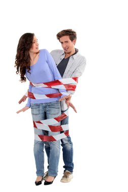 Couple being forcibly held together by caution tape clipart