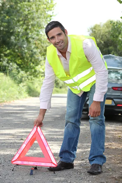 Hombre en chaleco fluorescente que emite un triángulo de advertencia por una avería —  Fotos de Stock