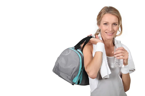 Blond kobieta noszenia odzieży sportowej, trzymając butelkę wody z torbą na ramieniu — Zdjęcie stockowe