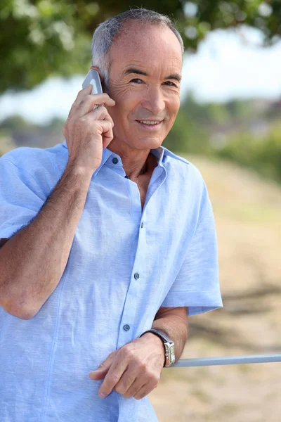 65 years old man at phone in front of a village — Stock Photo, Image