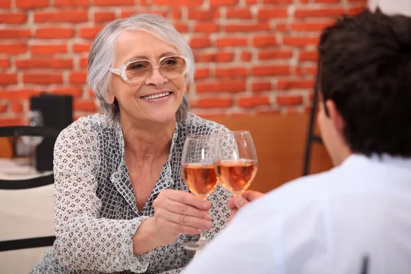 Older woman drinking rose wine in a restaurant with a young man — Stock Photo, Image