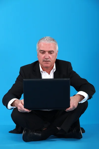 Senior-Geschäftsmann sitzt im Schneidersitz und hält einen Laptop — Stockfoto