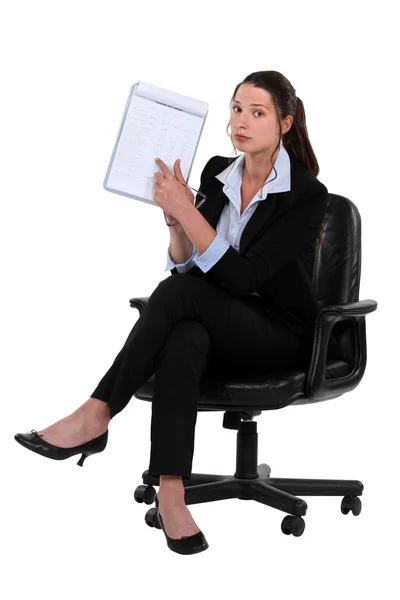Woman sitting on chair pointing at clipboard — Stock Photo, Image