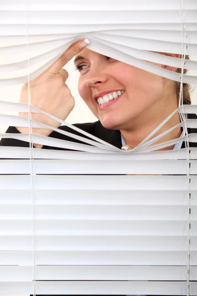 Nyfikna kvinnan tittar fram genom några persienner — Stockfoto