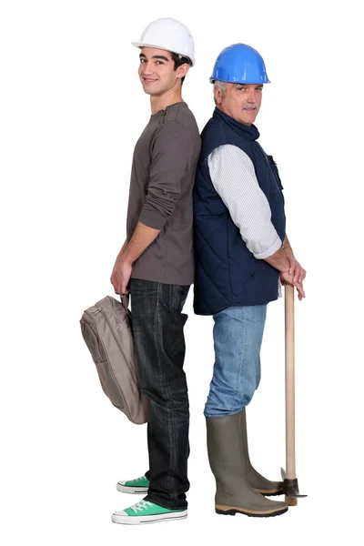 Senior craftsman and young apprentice standing back to back — Stock Photo, Image