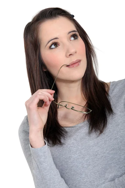 Aantrekkelijke vrouw met de arm van haar bril in haar mond — Stockfoto