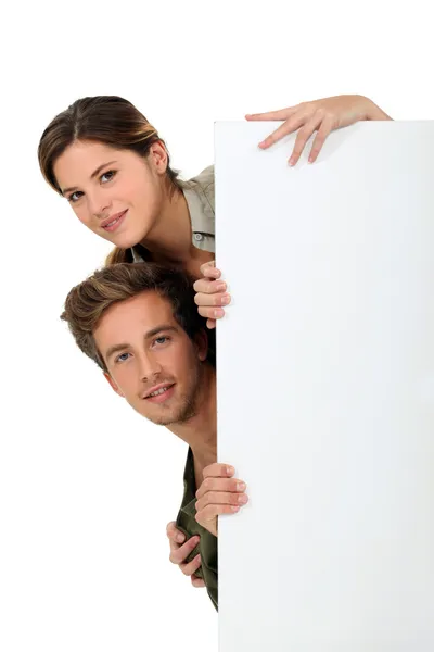 Homem e mulher espreitando atrás de um painel branco — Fotografia de Stock