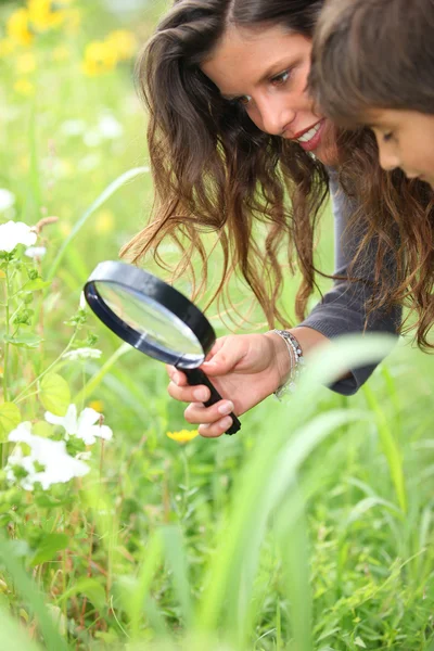 A woman and a little boy watching flowers with a magnifying glass — Stock Photo, Image