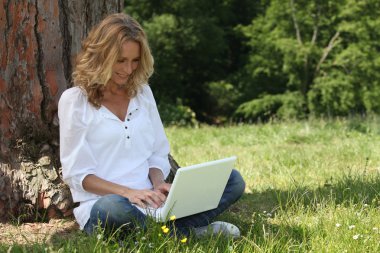 Woman laughing at her laptop computer in the park clipart