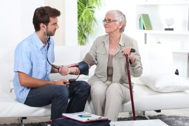 Young man taking the blood pressure of an older lady clipart