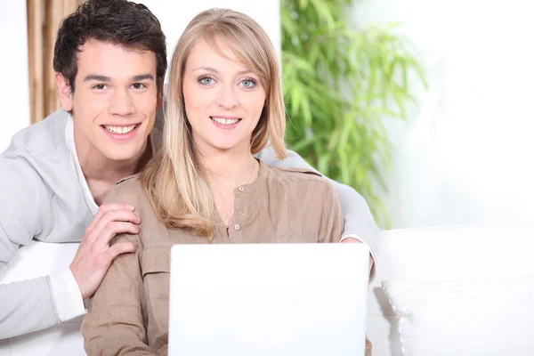 Casal jovem usando um computador portátil dentro de casa — Fotografia de Stock