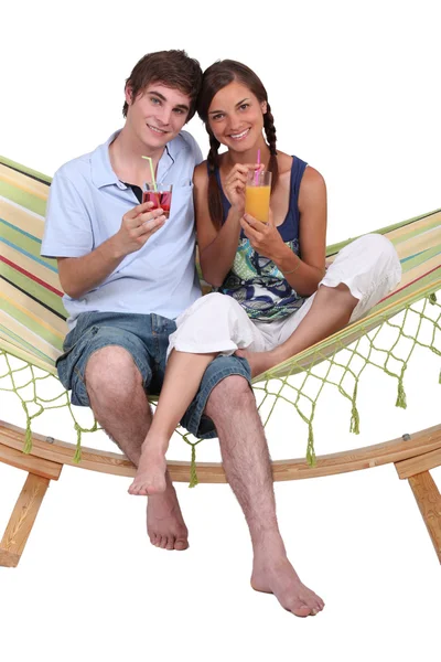 Unga par som sitter i hängmatta med drinkar — Stockfoto