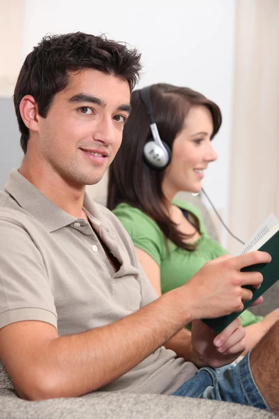 Mann liest, während seine Freundin Musik hört — Stockfoto