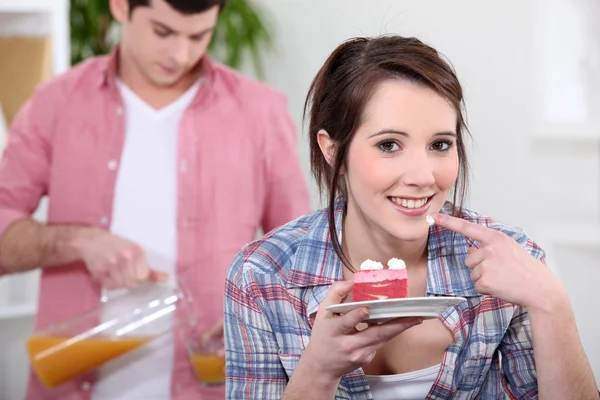 Girl eating strawberry gateau with boyfriend in background — Stock Photo, Image